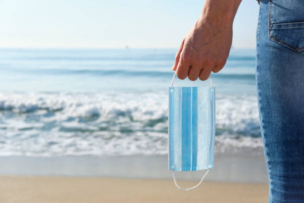 istock man with a surgical mask in his hand on the beach 1244755171