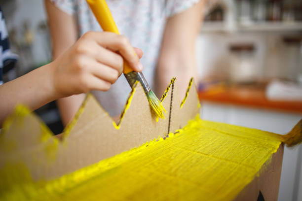 Hand of a Boy using paintbrush, painting carbdoard with yellow color