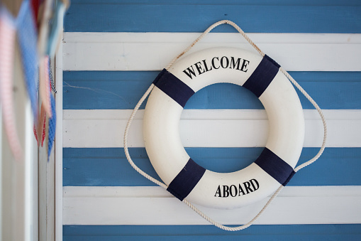 Navy and white lifebuoy ring with rope hung on a stripped blue and white wall as an welcome aboard sign with coloured bunting to one side