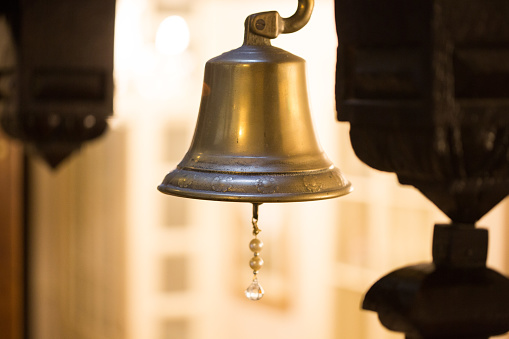 Close up of a brass bell with an ornate chime lit up by lighting in the background