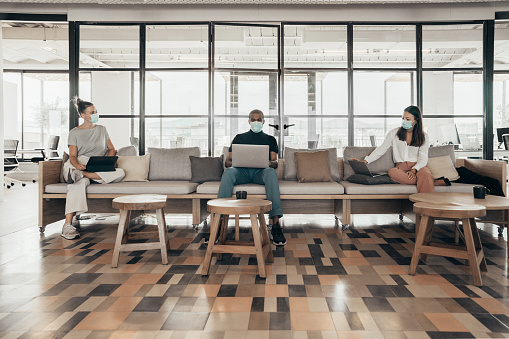 Empresarios que trabajan y mantienen la distancia social en un sofá en una oficina moderna photo