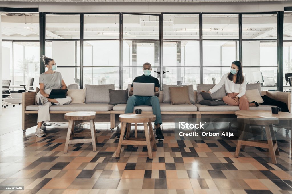 Businesspeople working and maintaining social distance on a sofa in a modern office Office Stock Photo
