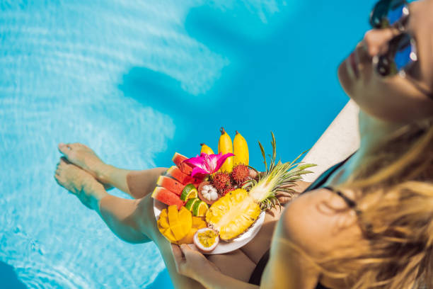 istock Young woman relaxing and eating fruit plate by the pool 1244795566