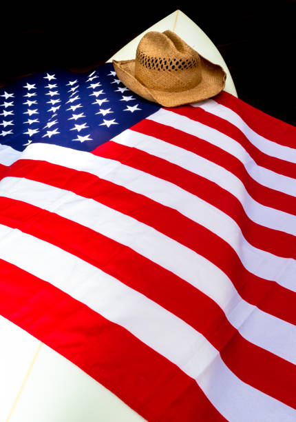 istock USA Flag on a white surfboard with a straw hat, black background, and a guitar. 1244821097