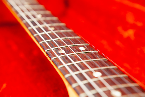 Close-up of an electric guitar neck with a rosewood fingerboard in a red fur lined guitar case with copy space