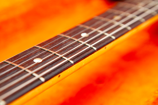 Close-up of an electric guitar neck with a rosewood fingerboard in an orange fur lined guitar case with copy space