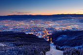 Town Liberec with winter mountain forest before sunrise. Czech early morning snow landscape pink and violet light. Snowy trees with fog, Jizerske hory, north of Bohemia, Czech republic. Light in town.