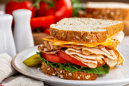 Closeup of turkey sandwich with cheese, tomato and lettuce on whole grain bread  with ingredients in blurred background
