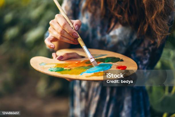 Close Up Hands Of Female Artist Holding Brush And Palette With Oil Paints Blurred Background With Easel In Sunflower Field Stock Photo - Download Image Now
