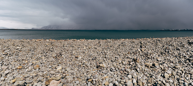 Stone pebbles on the beach in Reykjavik, Iceland. Panoramic views of the Atlantic Ocean, snow-capped mountains and cloudy skies in clouds. High quality photo