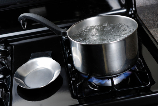 Water boiling in a stainless steal pot on a black stove.
