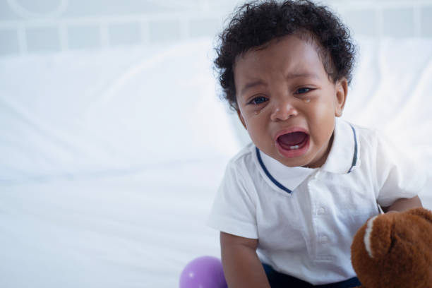 Cute nice little dark skinned baby boy crying on bed at home