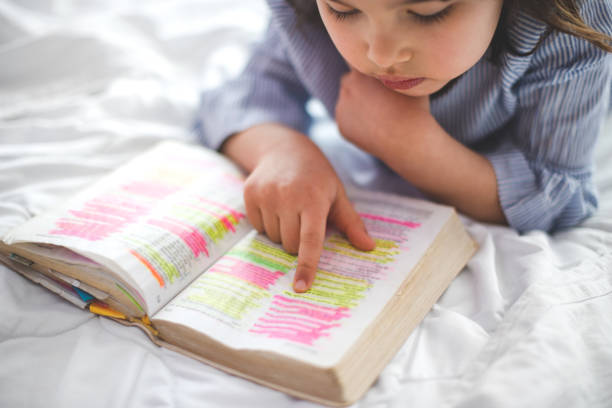 Little girl reading from Bible while lying in bed. The little girl reading from the Bible while lying in bed. stock photo