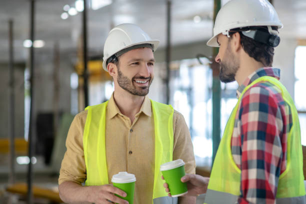 istock Building workers in yellow vests and helmets having coffee break, talking, smiling 1244892774