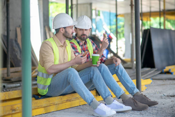 istock Building workers in yellow vests and helmets sitting on boards, having coffee with sandwiches, discussing something 1244892804