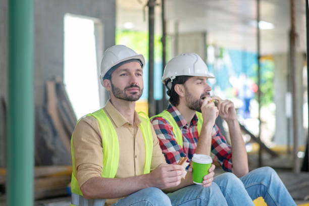 istock Building workers in yellow vests and helmets sitting, having coffee with sandwiches 1244892808