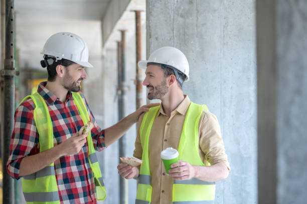 istock Building workers in yellow vests and helmets having coffee with sandwiches, talking, smiling 1244892813