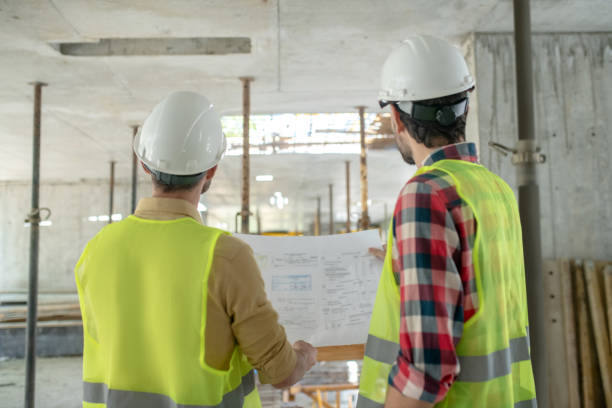 istock Building workers in yellow vests standing back to camera, holding blueprint, checking it 1244893912