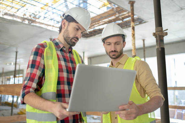 istock Building workers in yellow vests holding laptop, checking something on it 1244893940