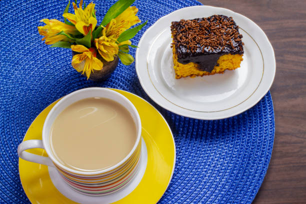 黄色い花で飾られた木製のテーブルにコーヒーとチョコレートアイシングとミルクのカップとニンジンケーキ。 - cake yellow sweet food banquet ストックフォトと画像
