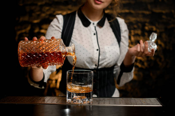 Close-up barman lady carefully pours alcoholic drink from bottle into glass