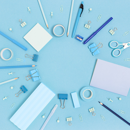 Round frame made of school supplies on a blue pastel background. Monochrome creative concept with copy space.