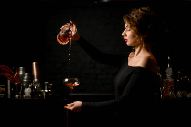 Woman bartender in dark bar masterfully pours cocktail into wineglass.