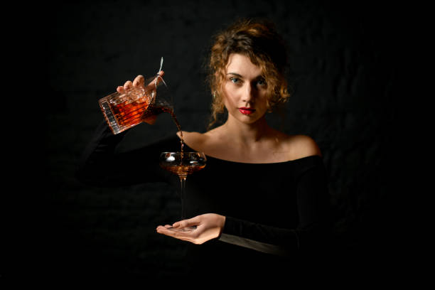 professional woman bartender holds glass in her hand and pours cocktail into it