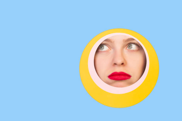 istock Female face with red lips peeking throught circle in blue background 1244934167