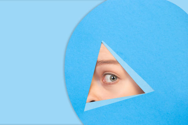 istock Female eye looking, peeking throught triangle in blue background 1244934170