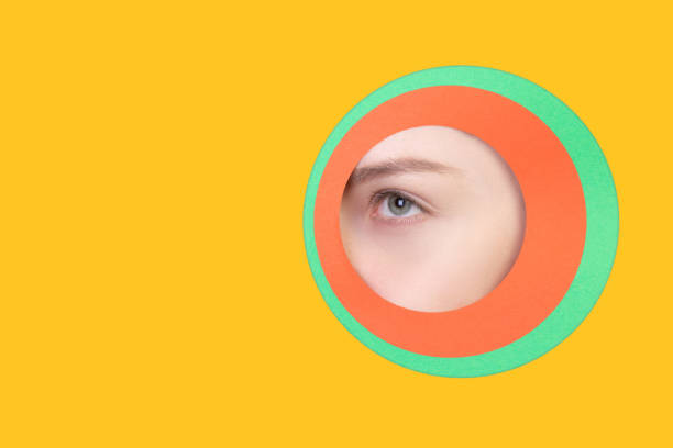 istock Female eye peeking throught circle in yellow background 1244934171