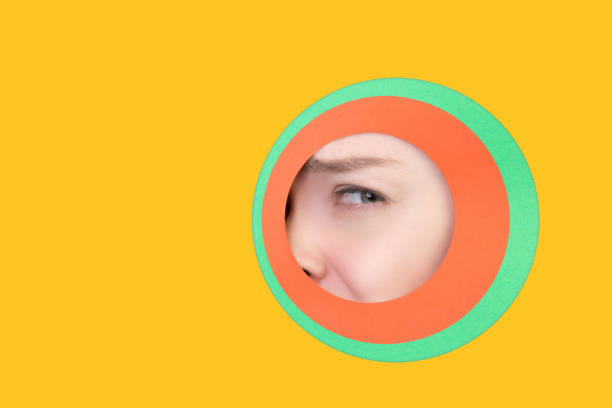 istock Female eye peeking throught circle in yellow background 1244934175