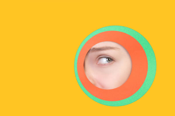 istock Female eye peeking throught circle in yellow background 1244934177