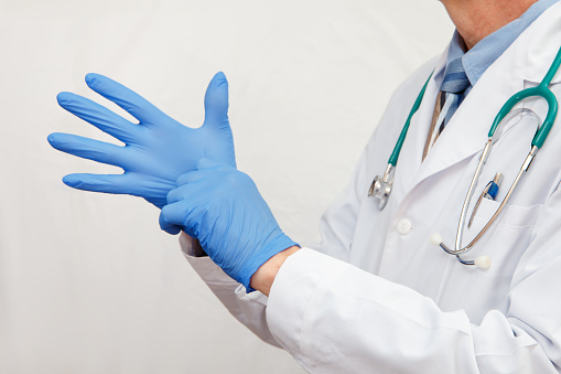 The doctor in a white coat puts on protective gloves. Healthcare concept