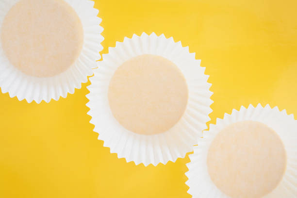 istock white cupcakes paper packaging background. cupcake foil on yellow background. cupcake cups, rolling pin, whisker. Happy food concept. Baking concept. 1244963825