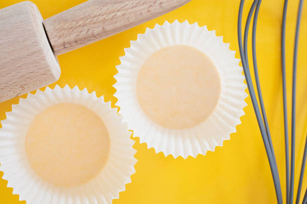 istock white cupcakes paper packaging background. cupcake foil on yellow background. cupcake cups, rolling pin, whisker. Happy food concept. Baking concept. 1244964405
