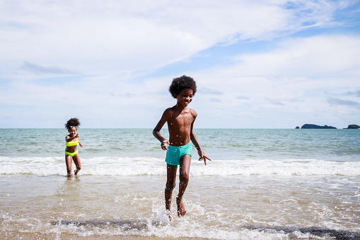 African American friendship in swimwear enjoying running to play the waves on beach. Ethnically diverse concept. Having fun after unlocking down from COVID 19. Summer holidays on beach with friends