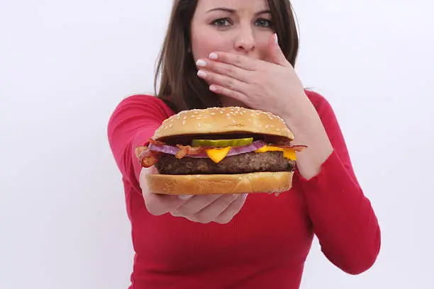 focus is on the cheeseburger as a girl in the background holds it out before her