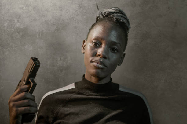 retrato de estilo cinematográfico de hollywood de joven atractiva y segura de sí misma mujer afroamericana negro sosteniendo el arma como agente federal especial o mafioso apuntando la pistola - gun women handgun armed forces fotografías e imágenes de stock