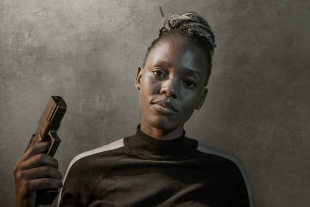 retrato estilo filme hollywoodiano de jovem atraente e confiante mulher negra afro-americana segurando arma como agente federal especial ou mafioso apontando a arma - gun women handgun armed forces - fotografias e filmes do acervo