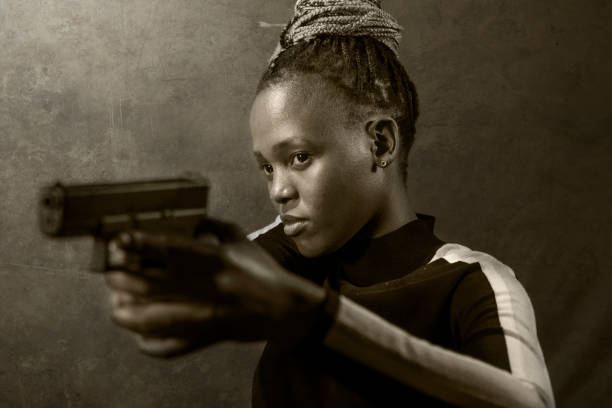 retrato de estilo cinematográfico de hollywood de joven atractiva y segura de sí misma mujer afroamericana negro sosteniendo el arma como agente federal especial o mafioso apuntando la pistola - gun women handgun armed forces fotografías e imágenes de stock