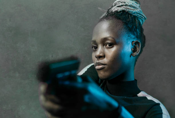 retrato estilo filme hollywoodiano de jovem atraente e confiante mulher afro-americana segurando arma como agente federal especial ou mafioso apontando a arma - gun women handgun armed forces - fotografias e filmes do acervo