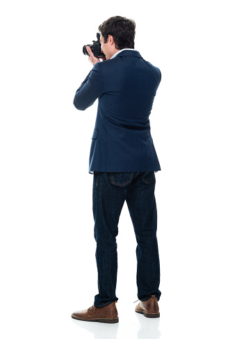 One person of aged 20-29 years old with short hair caucasian male photographer standing in front of white background wearing business casual who is photographing and holding camera