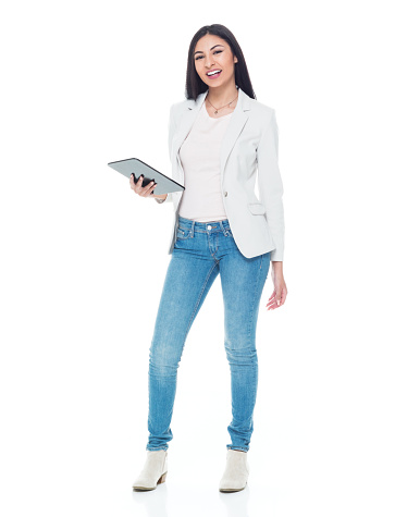 Front view of aged 20-29 years old who is beautiful latin american and hispanic ethnicity young women standing in front of white background wearing jacket who is cheerful and using digital tablet