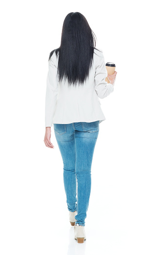 Rear view of aged 20-29 years old who is beautiful latin american and hispanic ethnicity female walking in front of white background wearing jacket who is showing cool attitude and holding coffee cup