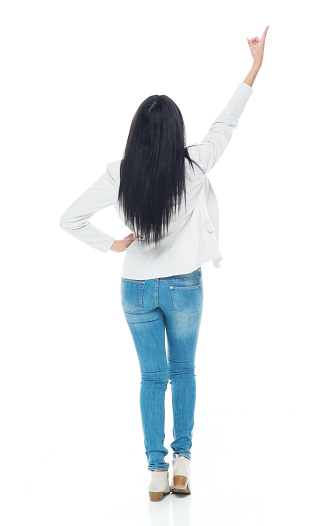 Rear view of aged 20-29 years old who is beautiful latin american and hispanic ethnicity young women standing in front of white background wearing jacket who is showing cool attitude who is pointing