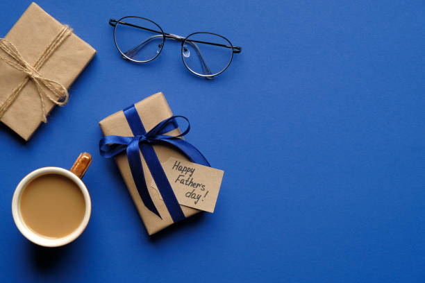 istock Happy Fathers Day concept. Flat lay composition with festive gift box, Happy Father's Day inscription, cup of coffee and glasses on blue background. Top view. 1245065008