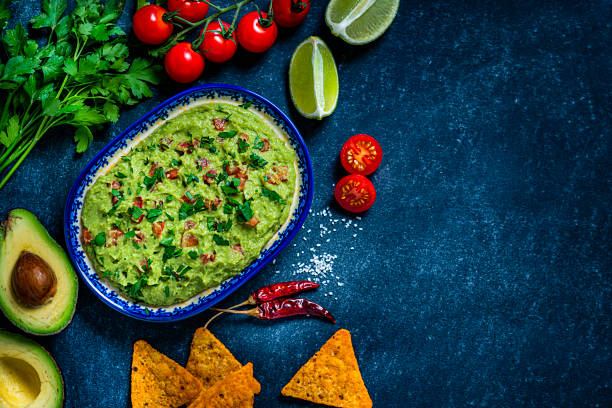 Guacamole and chips on bluish tint table. Copy space Mexican food: guacamole dipping sauce in a bowl with tortilla chips shot from above on abstract bluish tint table. Ingredients for preparing guacamole are all around the bowl and includes ripe avocados, tomatoes, lime, cilantro and salt. The composition is at the left of an horizontal frame leaving useful copy space for text and/or logo at the right.
Predominant colors are green and blue. High resolution 42Mp studio digital capture taken with Sony A7rII and Sony FE 90mm f2.8 macro G OSS lens guacamole photos stock pictures, royalty-free photos & images