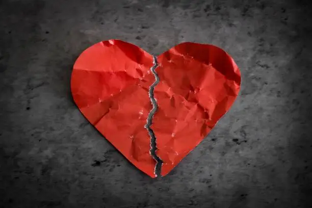 Red paper heart ripped in half on dark background. Broken heart separation concept