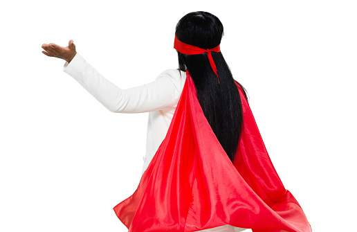 Rear view of aged 20-29 years old who is beautiful with black hair latin american and hispanic ethnicity young women presenter standing in front of white background wearing cape - garment who is conquering adversity who is showing with hand presenting
